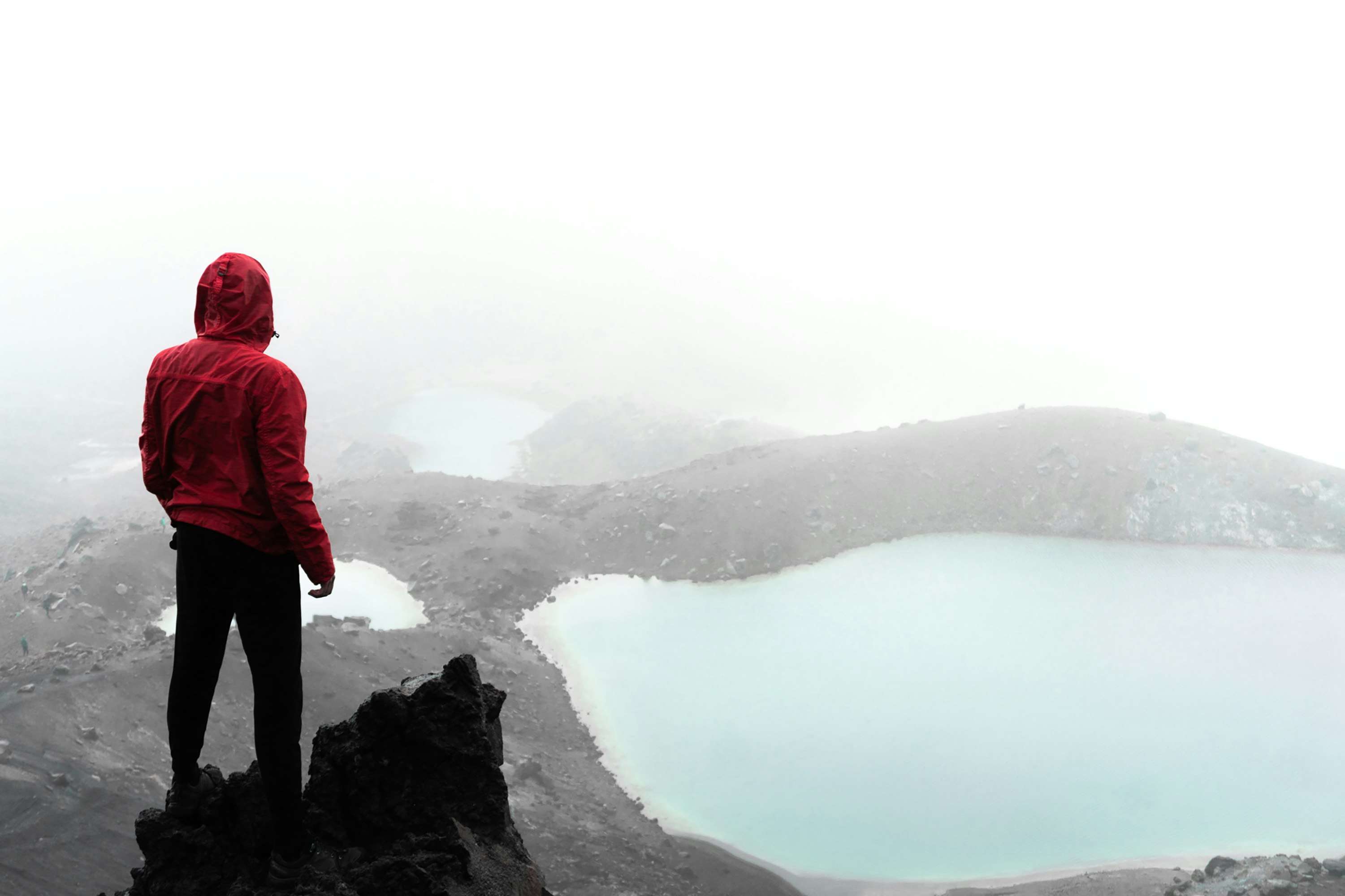 person in red hoodie standing on rock formation near body of water during daytime